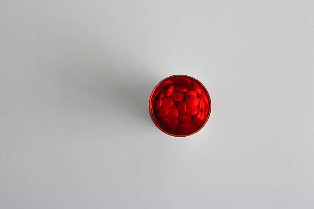 Close-up and selective focus on red pills in amber bottle placed on white wooden table, high angle view