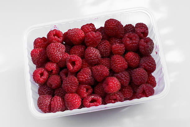 A generous assortment of fresh, plump raspberries fills a transparent container, showcasing their vibrant red color and inviting texture. Perfect for snacks or desserts.