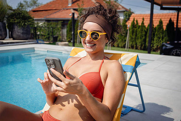 istock Woman relaxing poolside while browsing smartphone in casual summer outfit 2233824083