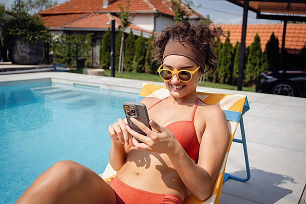istock Woman relaxing outdoors by poolside with smartphone and summer attire 2233824285