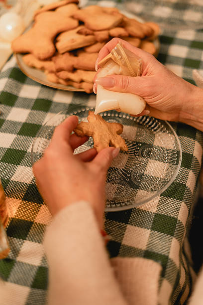Hands delicately adorn a gingerbread man with white icing, capturing a cozy, inviting atmosphere. Ideal for holiday-themed content, baking websites, or family-centered festive promotions this season.