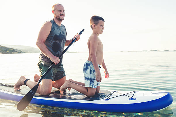 istock Father and son are having fun while enjoying together on a paddleboard on the sea at sunset. They are having precious moments together while enjoying their summer adventure. 2233827401