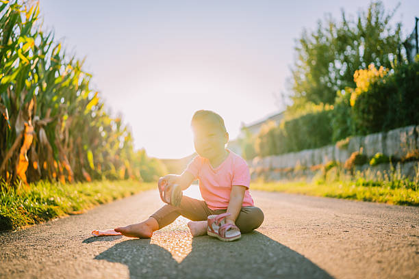 Young child sitting on paved street during golden hour, holding a shoe in hand. Outdoor candid lifestyle scene in Germany.