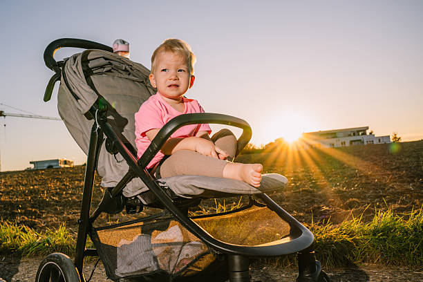 Child seated in a stroller during golden hour sunlight with rural and residential background in Germany. Outdoor candid lifestyle photo.