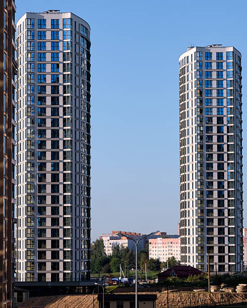 istock Twin apartment buildings, with repeating window patterns and light gray exteriors, rise above the city landscape under a bright, cloudless blue sky 2233831336