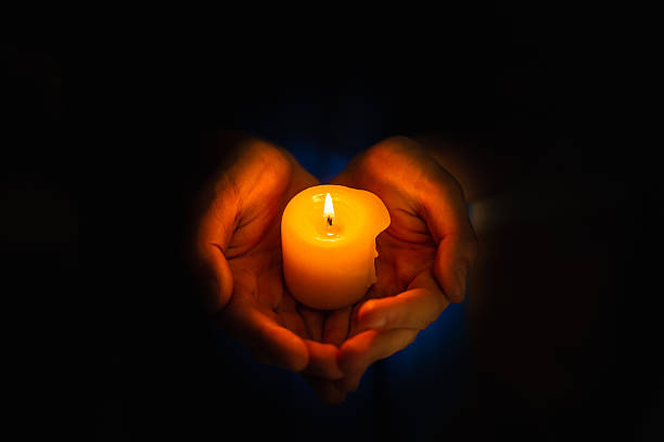 istock Hands holding burning candle in darkness like a heart, black background. 2233832572