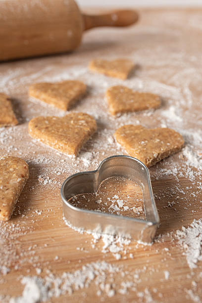 Homemade heart-shaped dog biscuits on a floured wooden surface with a metal cookie cutter and rolling pin in the background.