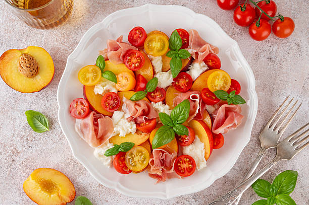 istock Salad with mozzarella, peaches, prosciutto ham, tomatoes and fresh basil on a white plate on a concrete background. Top view, copy space. 2233832871
