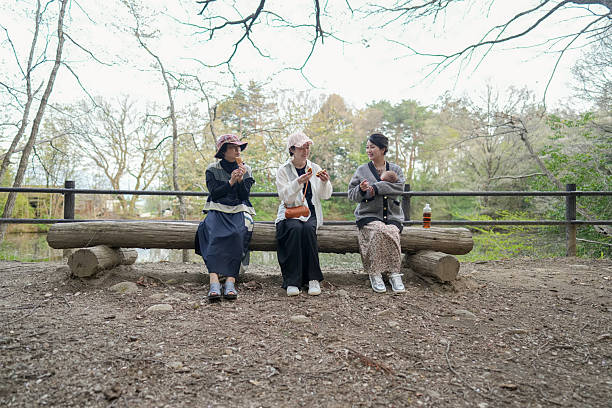 Three women sitting on a log in a park. One of them is holding a bottle. Scene is peaceful and relaxing