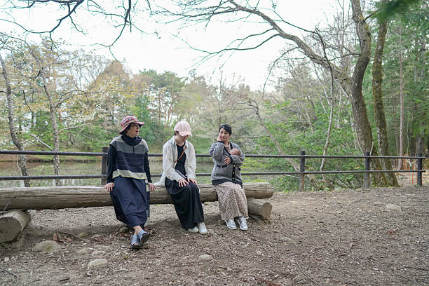 Three women sit on a log in a park. One of them is holding a baby. Scene is peaceful and relaxing
