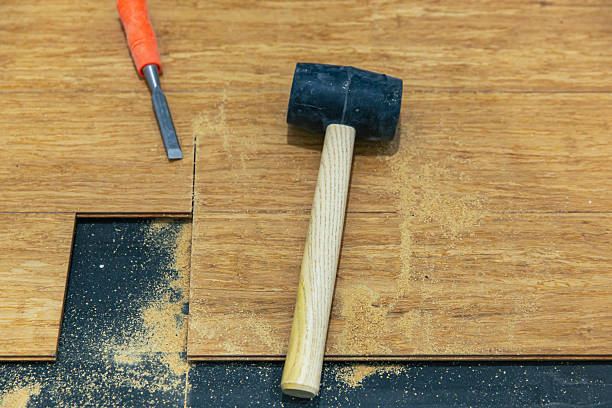 istock Wood floor repair with rubber mallet and chisel on engineered planks cut section sawdust 2233837196