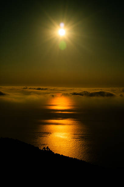 Sunlight casts a warm golden hue across the calm ocean, creating a shimmering pathway on the water. A mountain view adds depth to this peaceful evening atmosphere.