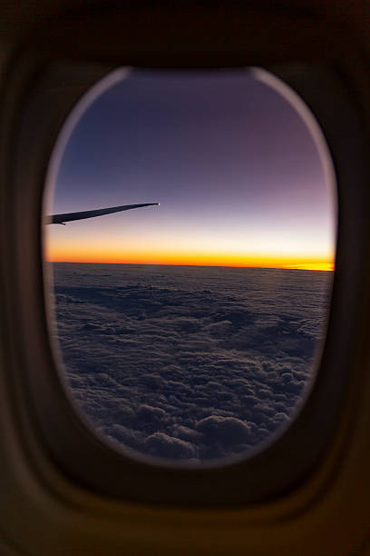 Airplane wing seen through window at sunrise above cloud blanket glowing wingtip vivid horizon tones
