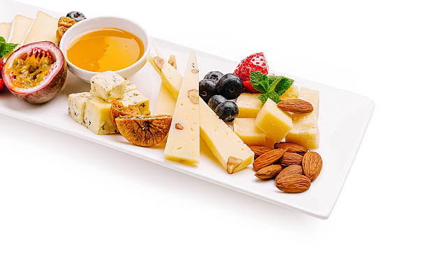 Delicious cheese platter with fruits, nuts, and honey on a white tray
