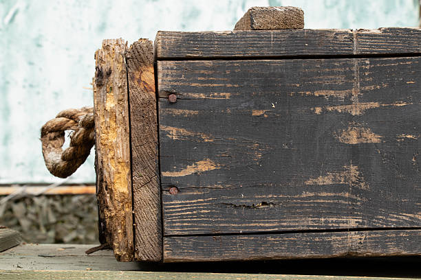 An old wooden box with worn black paint and rusty nails, with a rope handle visible on the side on the topic of army supplies and storage and transportation of weapons