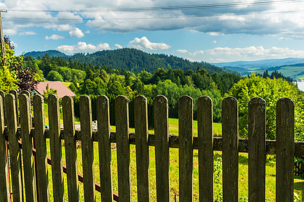 Rural path winding through green spring forest in Asturias, Spain, leading past an aged wooden fence and an old stone and tile roof house, symbolizing rustic charm and quiet village life