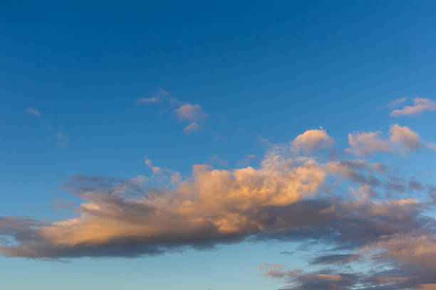 Warm light from the setting sun illuminates scattered clouds drifting across a clear blue sky in a peaceful evening scene