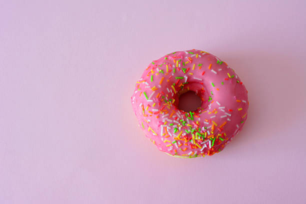 istock Pink frosted donut with colorful sprinkles on a pink surface copy space 2233857119