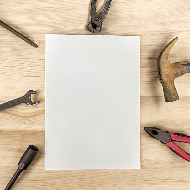 A blank white sheet framed by tools on a wooden surface. Symbol of creativity, construction, problem-solving, planning and DIY concepts.