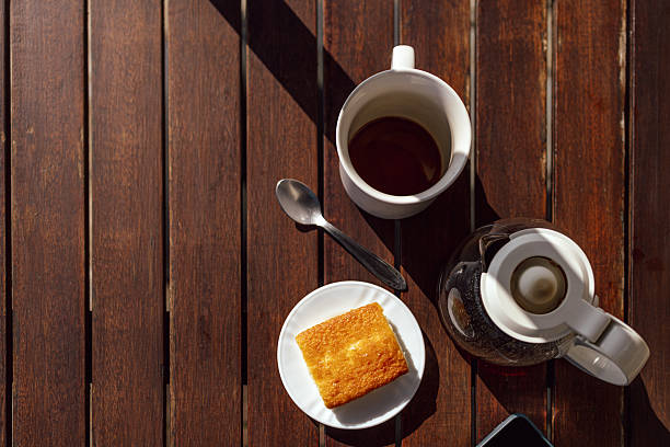 Coffee pot, cup and slice of pound cake on wooden table in sunlight