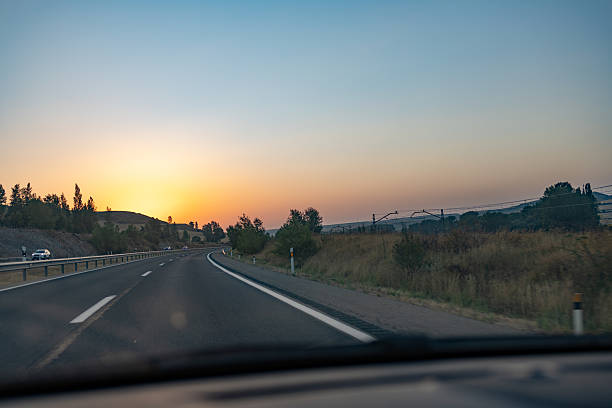 Alava province. Spanish basque country. Spain. The rising sun paints the sky with vibrant hues of orange and yellow as a car travels down an empty highway, marking the start of a new adventure