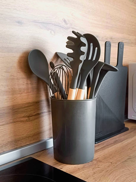 istock On the kitchen table there is a stylish black utensil holder, which is completely filled with various black utensils for cooking and preparing food. Close-up, vertical photo. 2233869151