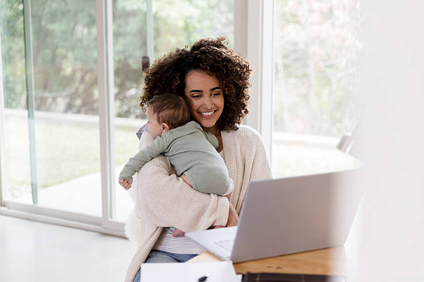 istock Working Mother Holding Baby, Using Laptop, Smiling 2233885110
