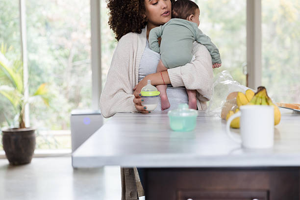istock Mother holding baby, preparing bottle, kitchen counter 2233885119