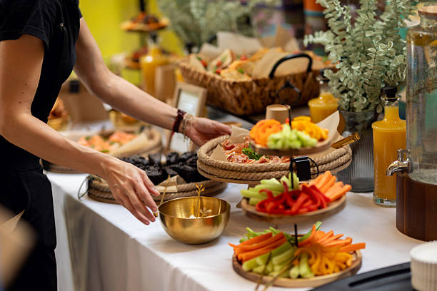 Caterer is setting up a buffet table with a variety of delicious food, including sandwiches, vegetables, and desserts Professional caterer arranging buffet with colorful sandwiches, fresh vegetables, and tempting desserts at catering event Corporate Events catering stock pictures, royalty-free photos & images