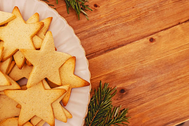 A plate of star-shaped cookies sits on a rustic wooden table, accented by sprigs of evergreen.