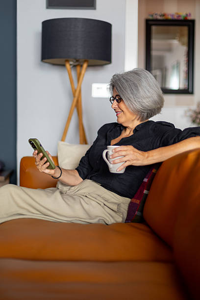 istock Senior woman relaxing on sofa using smartphone and drinking tea 2233918311