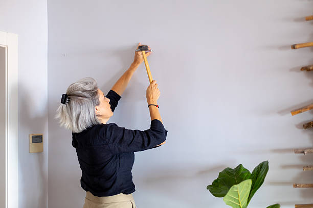 istock Woman hammering nail into wall at home 2233918351