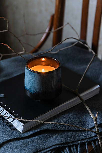 istock Lit candle in ceramic cup on notebook with branches and fabric, creating cozy wabi sabi atmosphere in soft natural tones. 2233920230