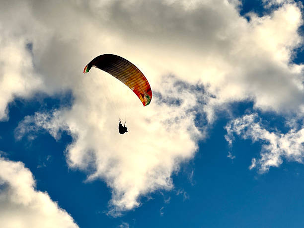 EX low angle para-glider in shilhouette against blue sky with clouds