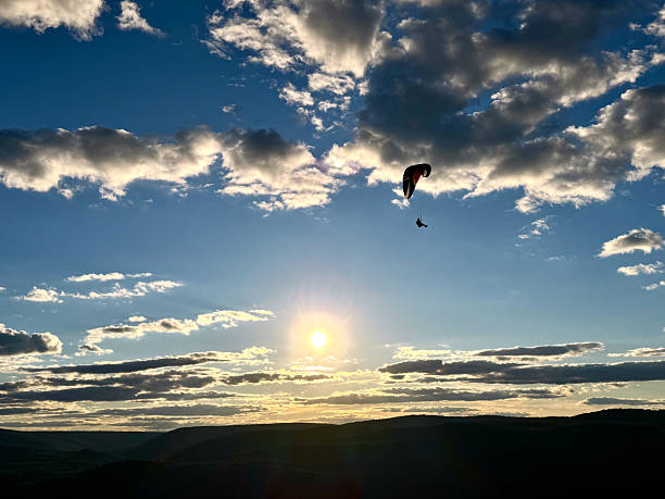 EX WS tiny para-glider silhouetted against blue sky with clouds, sun and valley below