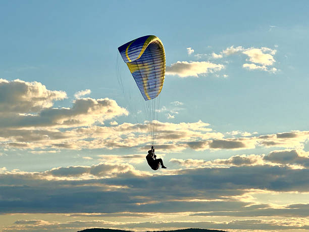 Para-glider with blue and yellow parachute in silhouette sails through blue skies