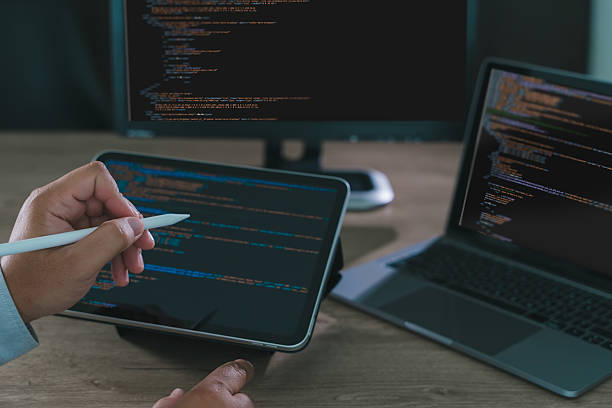 istock Close-up of programmer freelance working on tablet and laptop with code on screen, modern software development, coding, and remote work in home office environment. 2233926281