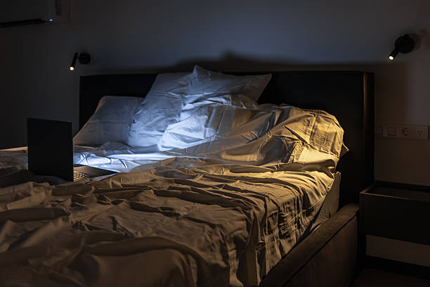 istock Overhead view of bed with lit laptop and contrast light. Night work. 2233939639