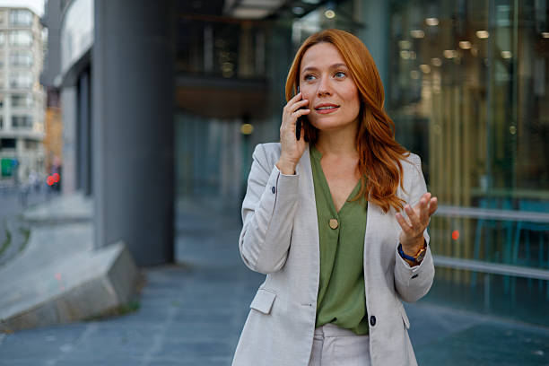 istock Confident businesswoman having a phone call while walking outside modern office building, gesturing and smiling 2233950833