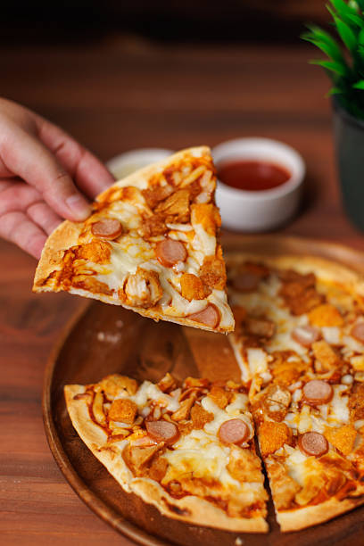 Hand lifts slice delicious melting tasty chicken and sausage crispy pizza with stretchy mozzarella cheese pull on wooden board homemade cooking ingredients lying on dark background, food advertisement