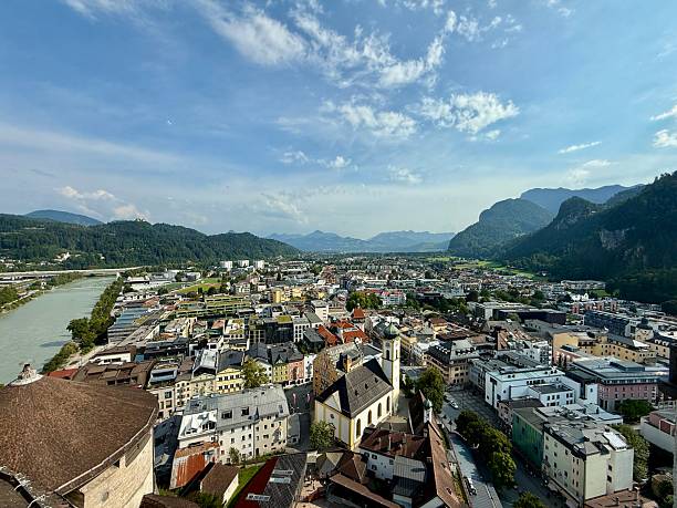 Caucasian middle aged tanned woman with electronic mobile audio tourist guide in hands stands against aerial view over Salzburg historic city center in Austria
