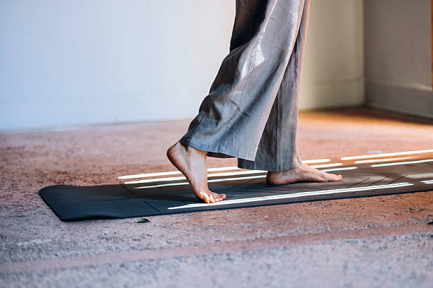 An individual practices yoga barefoot on a mat in a softly lit indoor setting, emphasizing mindfulness, balance, and tranquility, surrounded by sunlit tones and peaceful vibes.