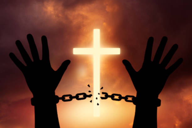Hands breaking free from chains with a glowing cross in the background, symbolizing spiritual freedom, salvation, and liberation through faith.