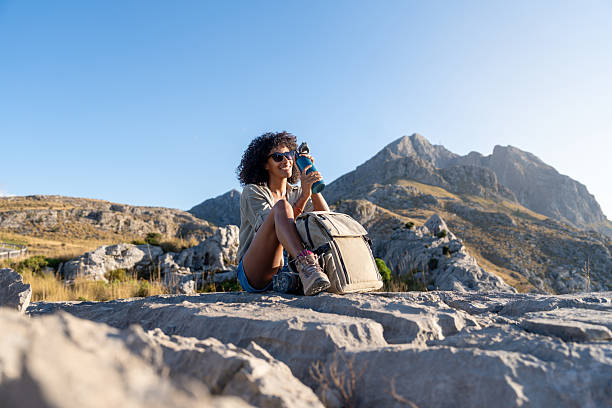 Young woman sits on rocks with backpack and bottle during a break in the Sierra de Tramuntana, Majorca. Concept of hiking, lifestyle, Balearic nature