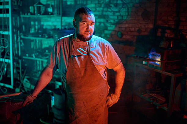 A mid adult Caucasian blacksmith is skillfully forging heated metal with a hammer in a traditional workshop. He is wearing protective gear and working with focus and precision, surrounded by industrial tools and glowing forge.