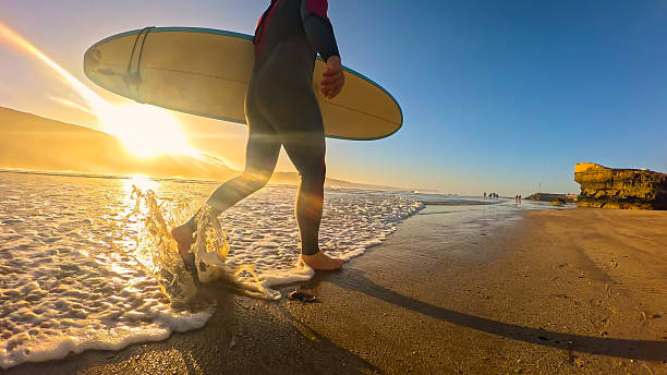 istock LOW ANGLE VIEW, LENS FLARE: Surfer walks along shoreline through shallow waves 2233966292