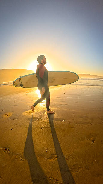 istock LENS FLARE, PORTRAIT: Young man in wetsuit is heading for morning surf session 2233966293