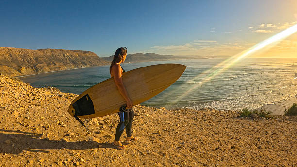 istock LENS FLARE, PORTRAIT: Woman with a surfboard walks along a scenic cliff path 2233966299
