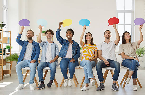 istock Positive diverse people sit in row and express their opinion by raising colored speech bubbles. 2233987988