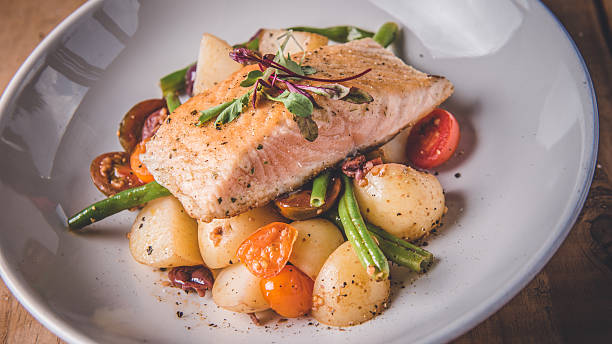 A savory plate featuring grilled salmon placed elegantly atop roasted potatoes, cherry tomatoes, green beans, and a sprinkle of herbs, creating a delightful and wholesome dining experience.